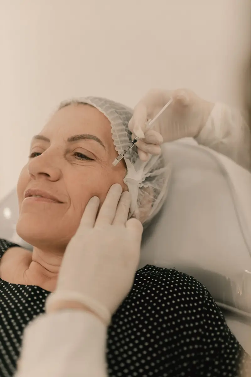 Mujer sonriente y relajada, con los ojos cerrados, durante un tratamiento facial inyectable