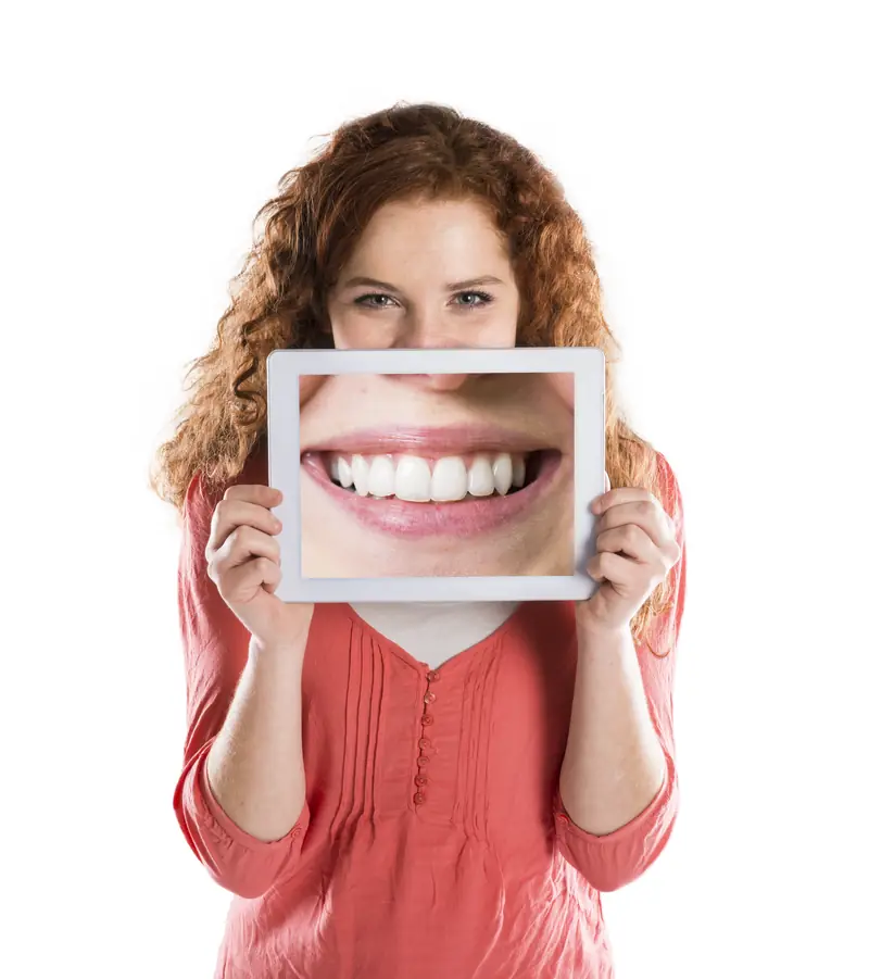 Mujer sostiene una tableta con la imagen de una sonrisa blanca delante de su boca