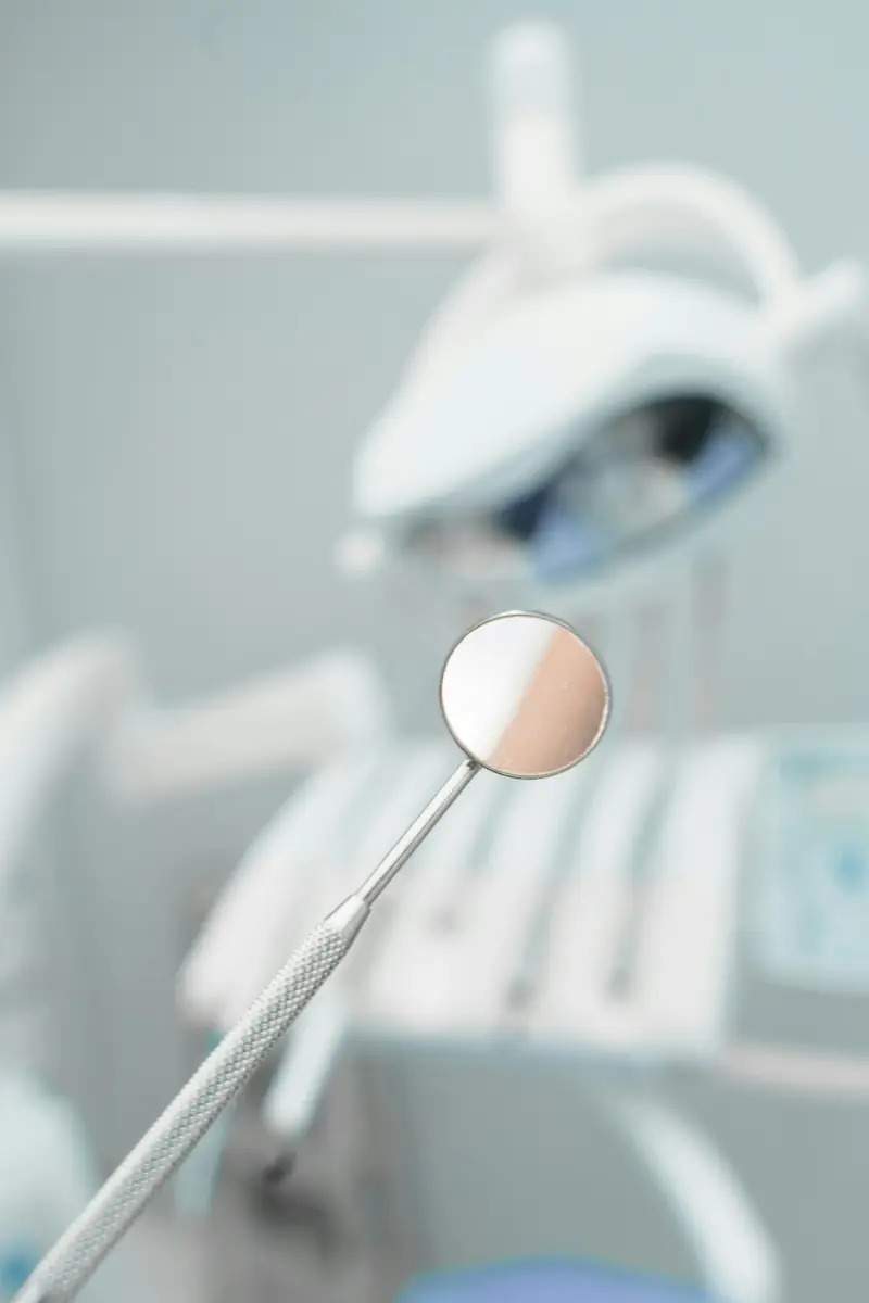 Espejo dental de exploración con el sillón del gabinete desenfocado al fondo