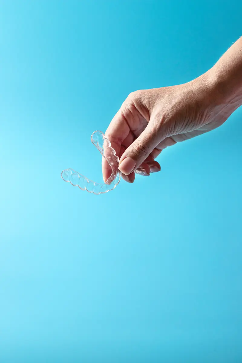 Mano sujetando un alineador transparente de ortodoncia invisible sobre fondo azul