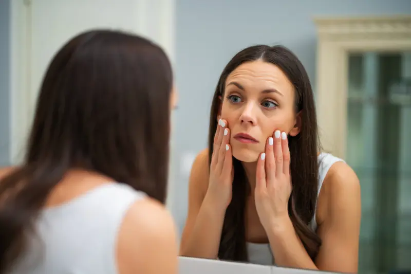 Mujer observa la piel de sus mejillas frente al espejo