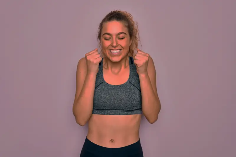 Mujer en ropa deportiva celebra con los puños cerrados y el abdomen tonificado
