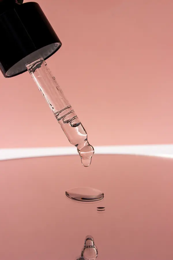 Gota de sérum cayendo de un cuentagotas sobre fondo rosa