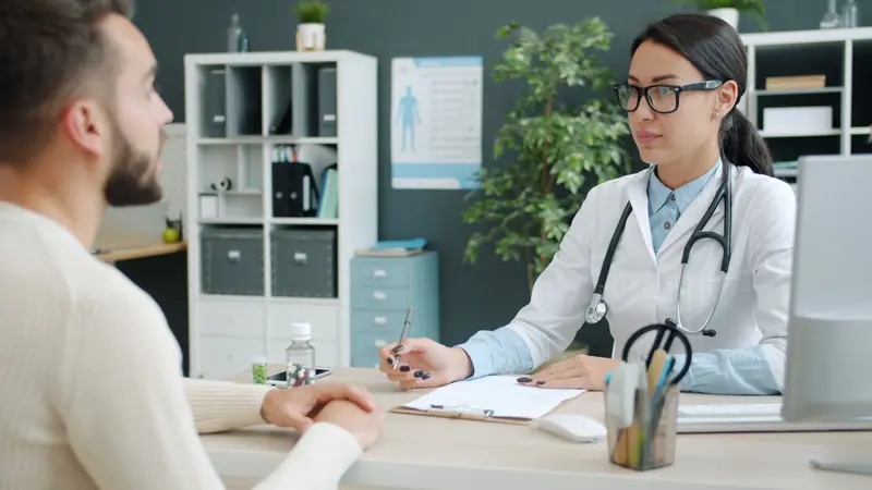 Médica toma notas durante la consulta con un paciente en un despacho luminoso