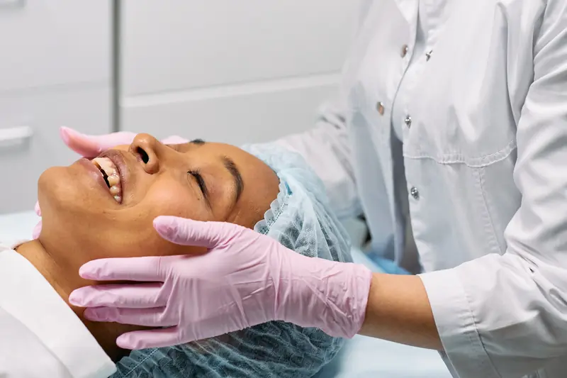 Especialista con guantes rosas realiza un tratamiento facial a una paciente relajada con los ojos cerrados