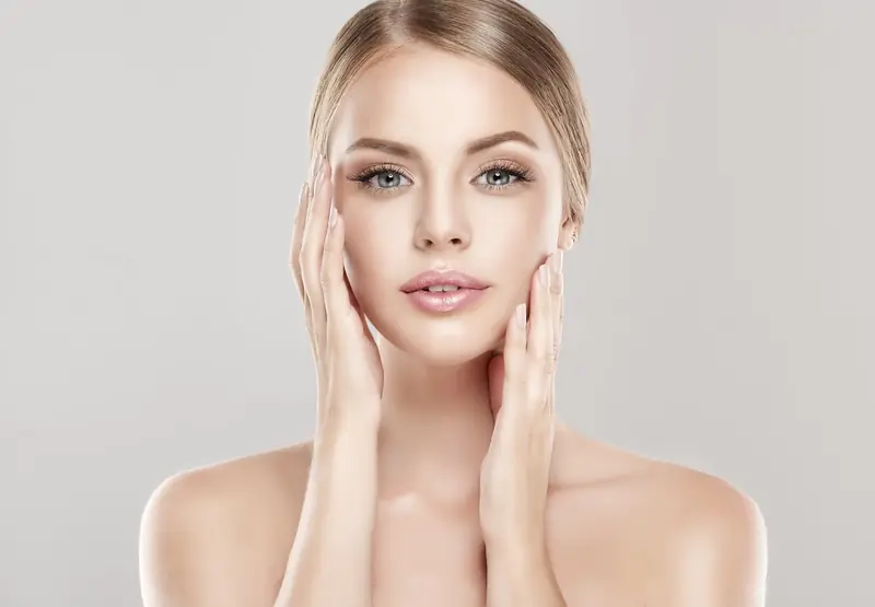 Mujer sonriente con los ojos cerrados y crema en el contorno de ojos